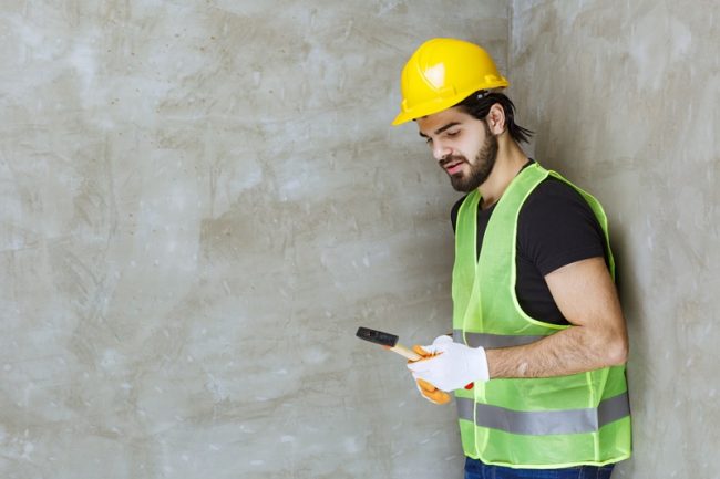 Engineer in yellow helmet and industrial gloves holding a metallic ax