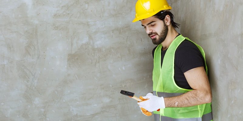 Engineer in yellow helmet and industrial gloves holding a metallic ax