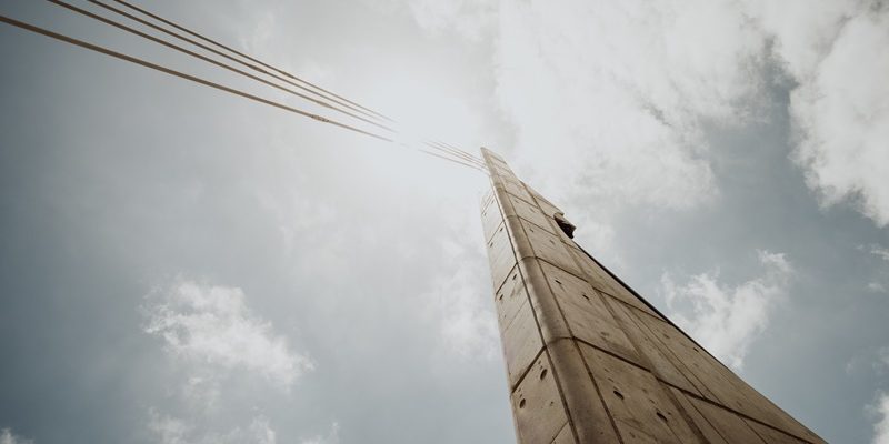 Low angle shot of a concrete column with cables against a bright cloudy sky